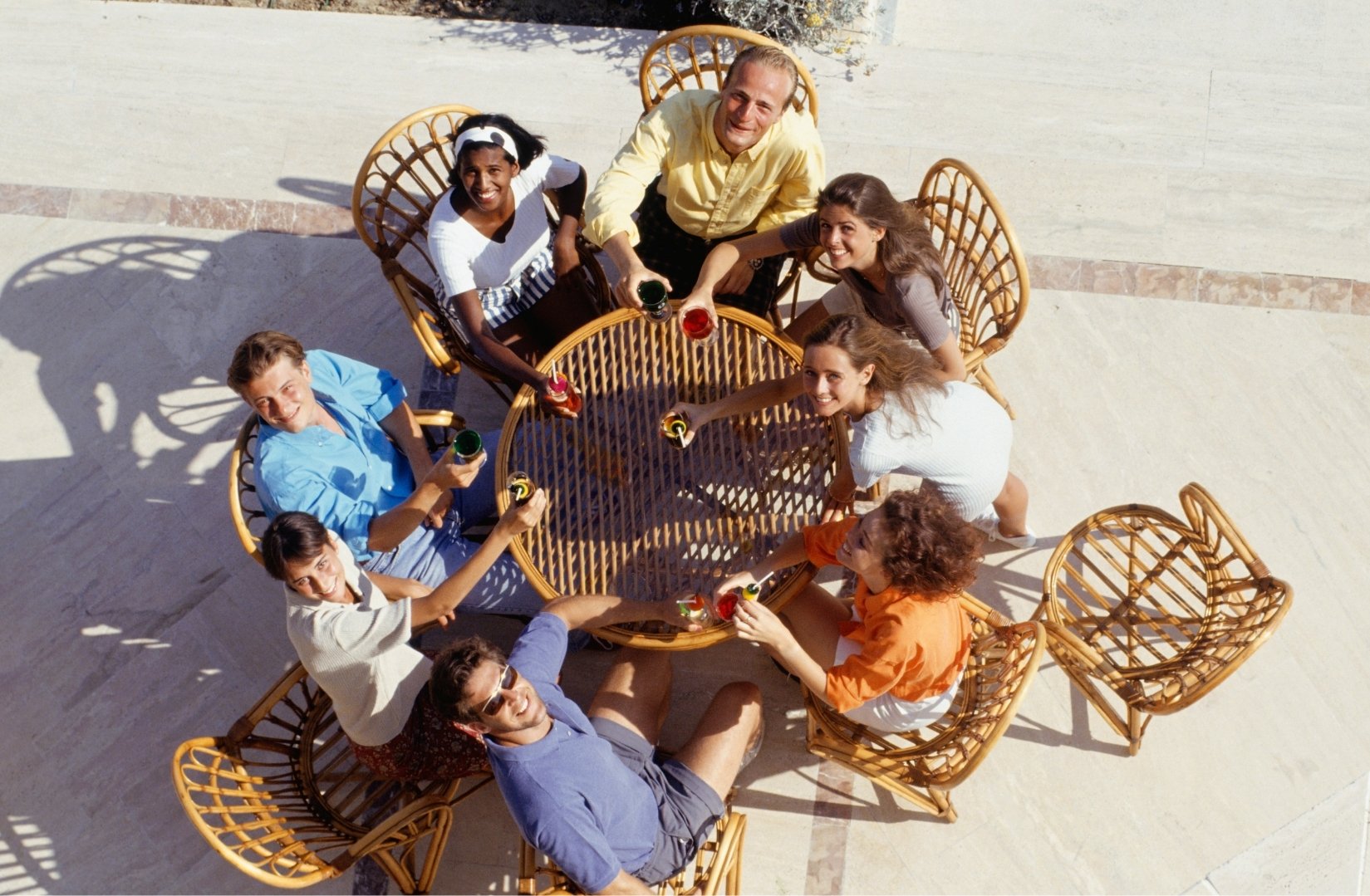 Groupe de collaborateurs en extérieur sous le soleil, installés autour d'une table avec des énigmes et des accessoires, ambiance décontractée et engagée, décor naturel avec végétation, lumière estivale chaude, canton de Vaud
