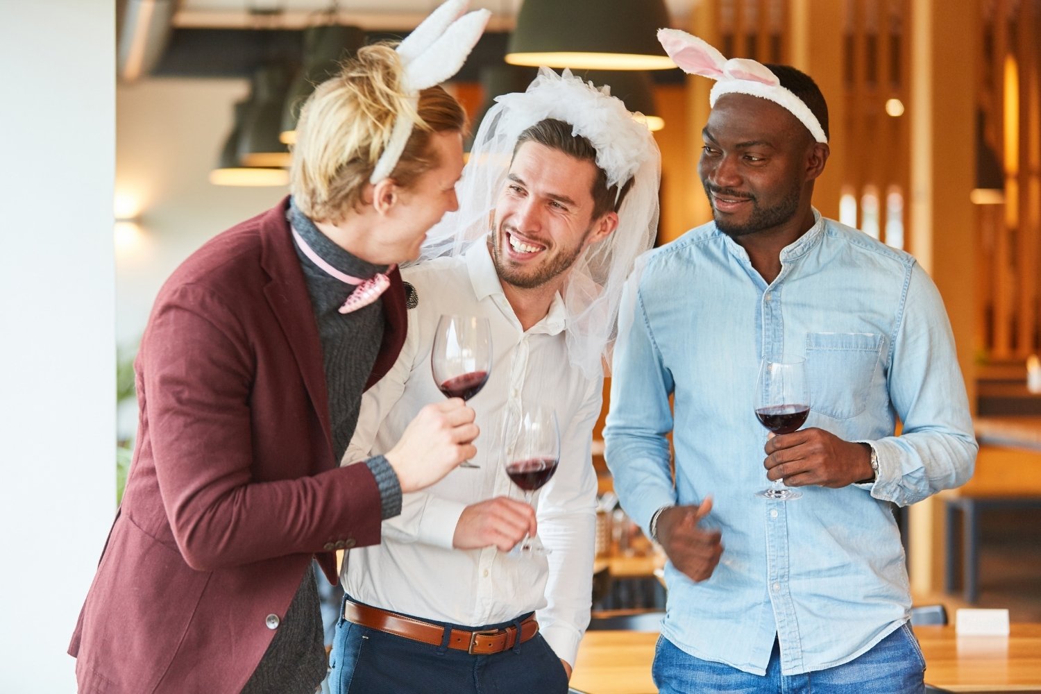 Groupe d'amis debout, verres à la main, célébrant la fin d'une session d'escape game, un membre du groupe portant un accessoire EVG/EVJF (écharpe, couronne), ambiance festive et chaleureuse, cadre d'appartement ou de terrasse lausannois.