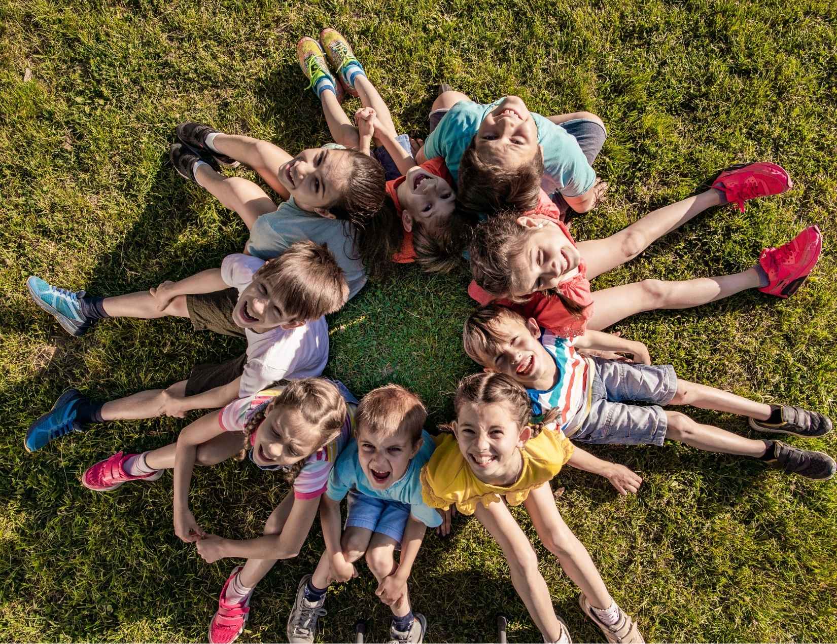 Groupe d'enfants d'âge primaire assis en cercle dans un espace extérieur ombragé de camp de vacances, penchés avec attention autour d'un coffre en bois ouvert rempli d'énigmes, un animateur accroupi à leurs côtés, ambiance lumineuse et concentrée.