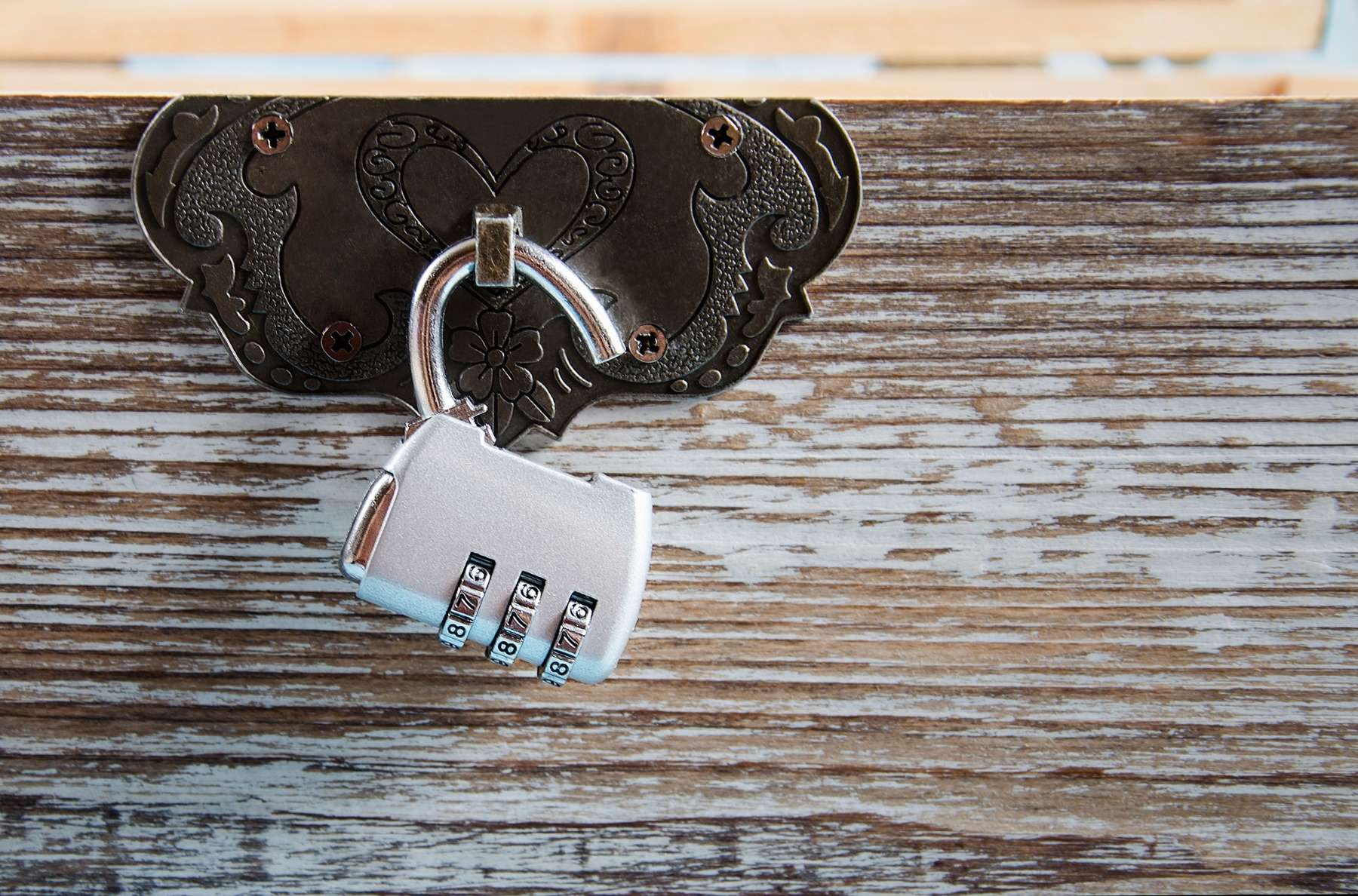 Gros plan sur les mains de deux collaborateurs manipulant un cadenas à combinaison fixé à un coffre en bois ancien, avec des cartes et un carnet ouvert à côté. Lumière chaude de fin de journée, faible profondeur de champ, ambiance mystère et concentration.