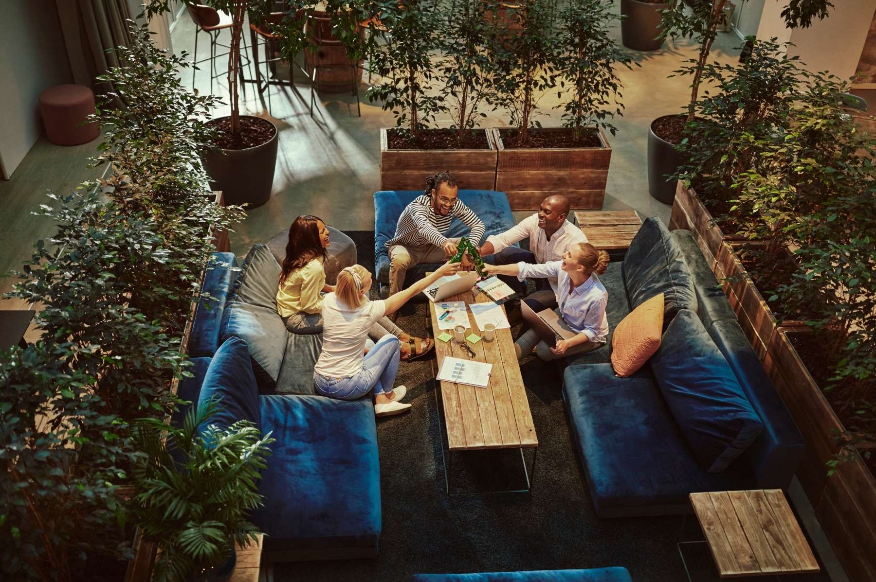 Un petit groupe de six collègues en extérieur, sur une terrasse d'entreprise en fin d'après-midi d'été, penchés sur un coffre en bois ouvert rempli d'objets d'énigmes. Verres d'apéritif posés à côté, lumière dorée rasante, expressions concentrées et rieuses.