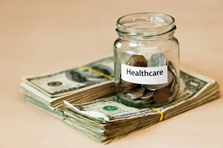 A glass jar with a sticker saying, "healthcare," on top of hundred dollar bills