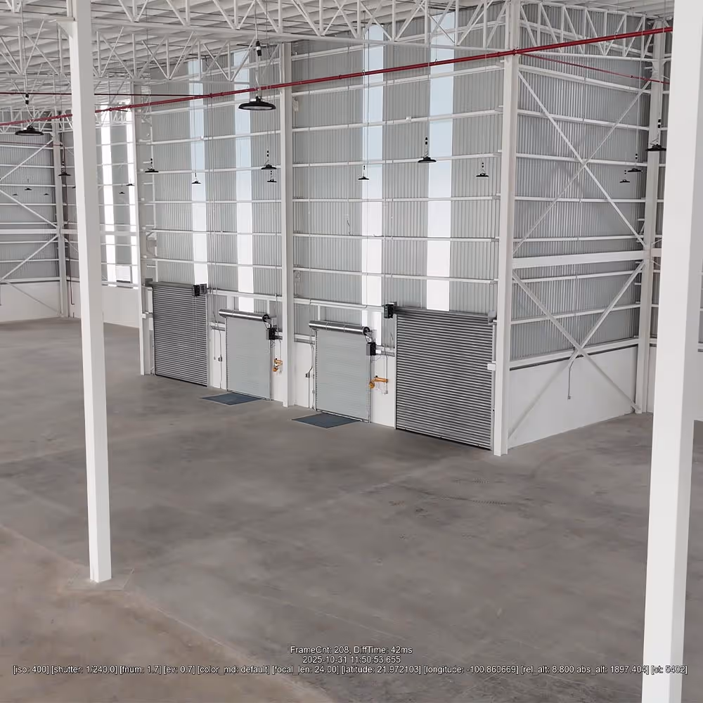 Interior de almacén industrial con piso de concreto, vigas estructurales blancas y cuatro puertas metálicas enrollables cerradas.