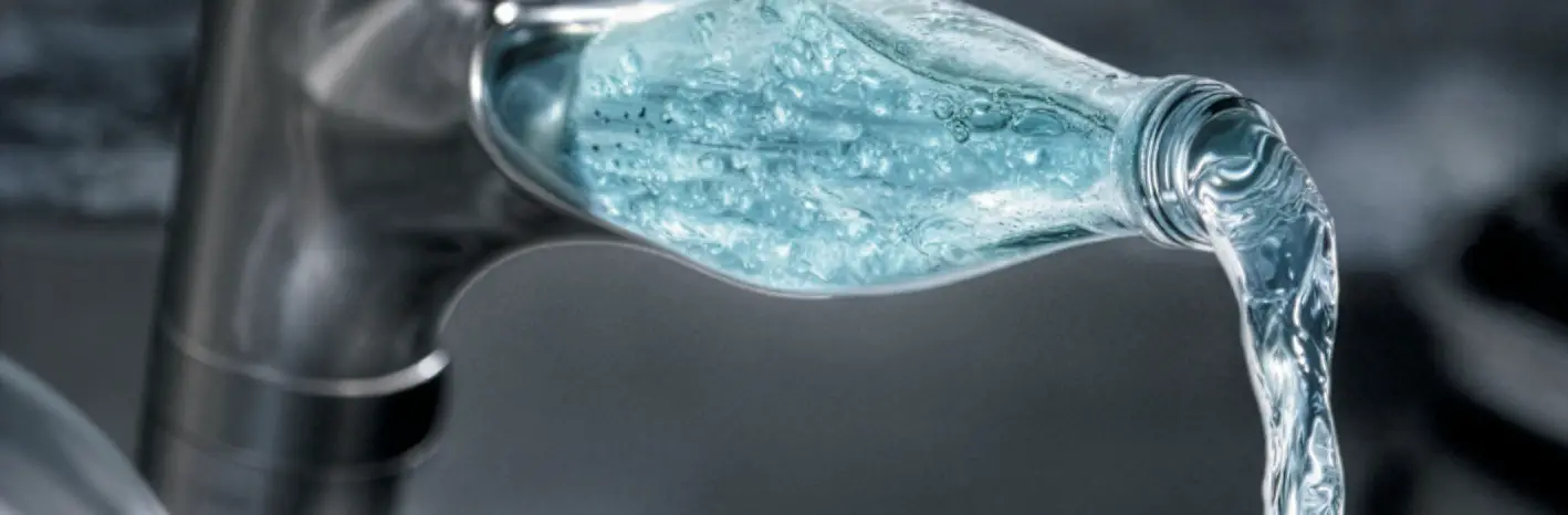Close-up of water pouring from a faucet with a splash shaped like a water bottle.