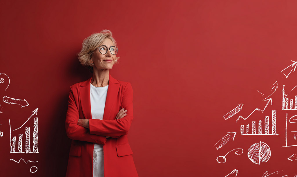 Confident senior professional woman with short blonde hair and glasses, wearing a red blazer and white shirt, standing with arms crossed against a red background with hand-drawn white charts and graphs, symbolizing leadership and data-driven strategy.