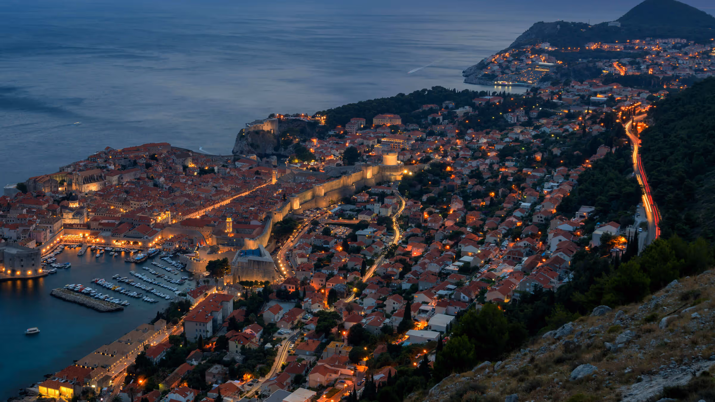 A coastal, Mediterranean town at dusk with warm glowing lights