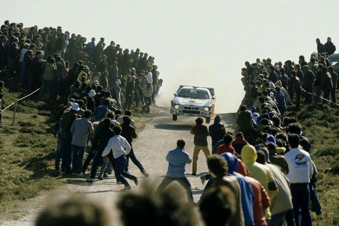 Une foule compacte bordant une route en gravier observe le passage d’une voiture du Groupe B pendant le Rallye du Portugal 1983
