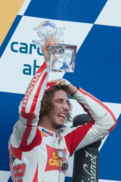 Marco Simoncelli brandissant son trophée sur le podium du Grand Prix, sourire éclatant.