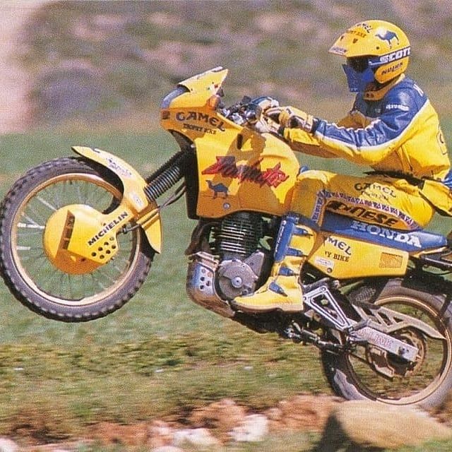 un pilote du camel trophy en moto avec une moto jaune dominator en wheeling