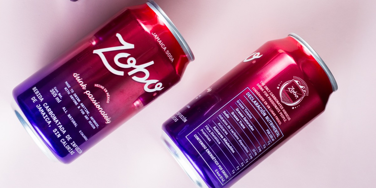 Two red and purple cans of Zoho Jamaica soda on a light surface, one showing the front label and the other the nutritional facts.