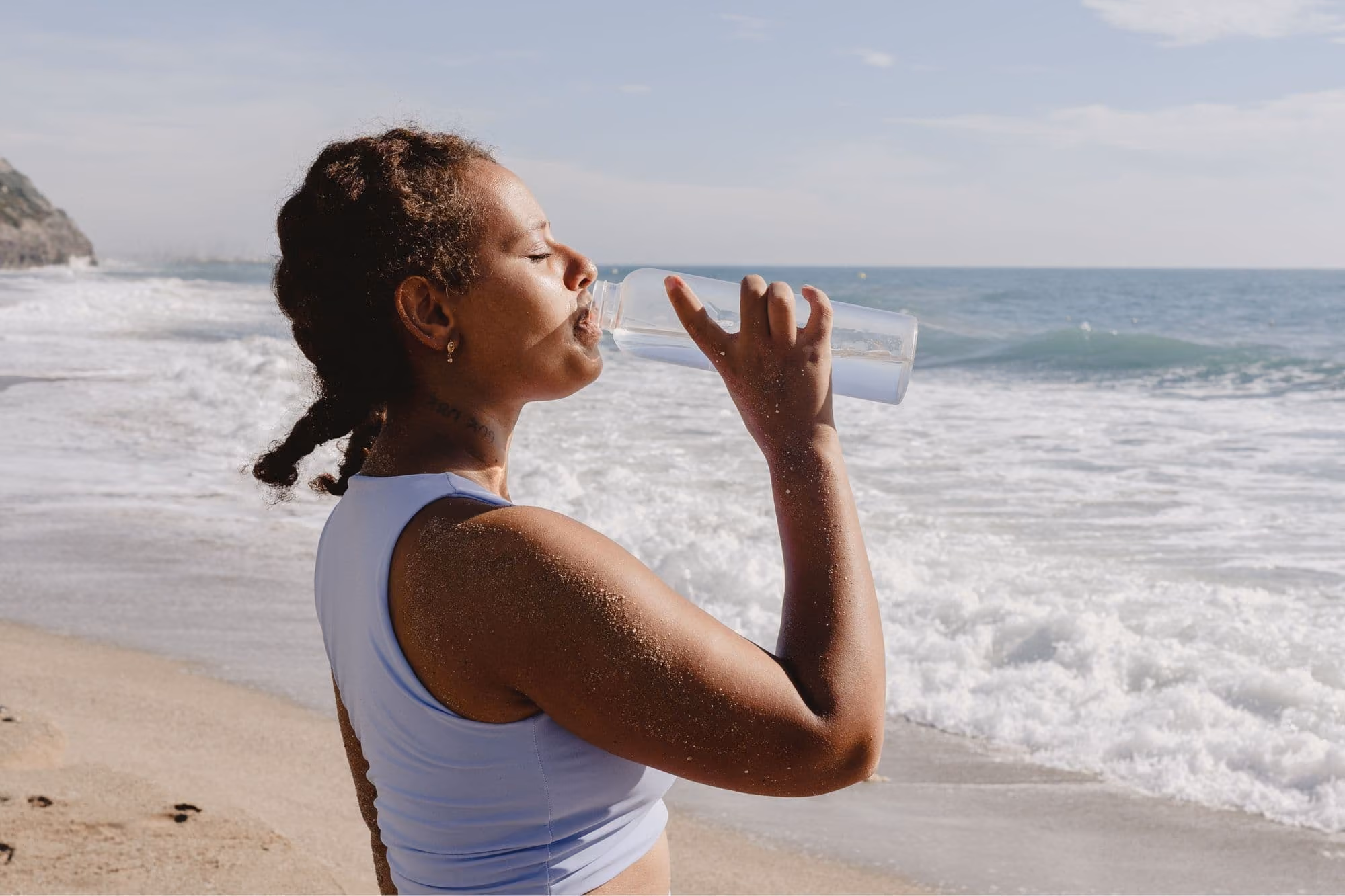 Mujer bebiendo agua en la playa representando bienestar y seguro de salud