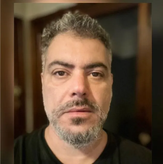 Middle-aged person with gray hair and beard looking directly at camera