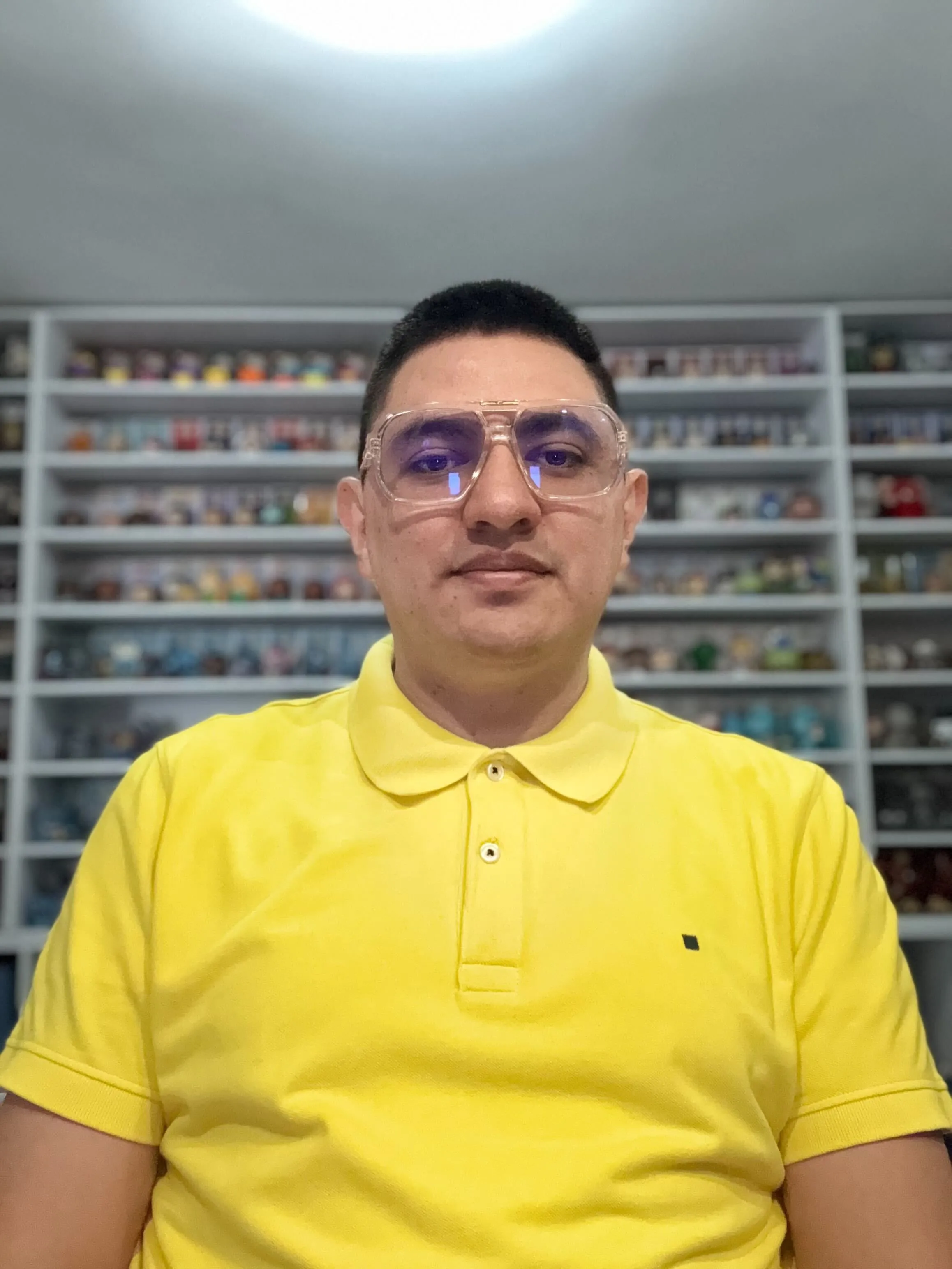 Person in yellow polo shirt wearing glasses standing in front of shelved collection