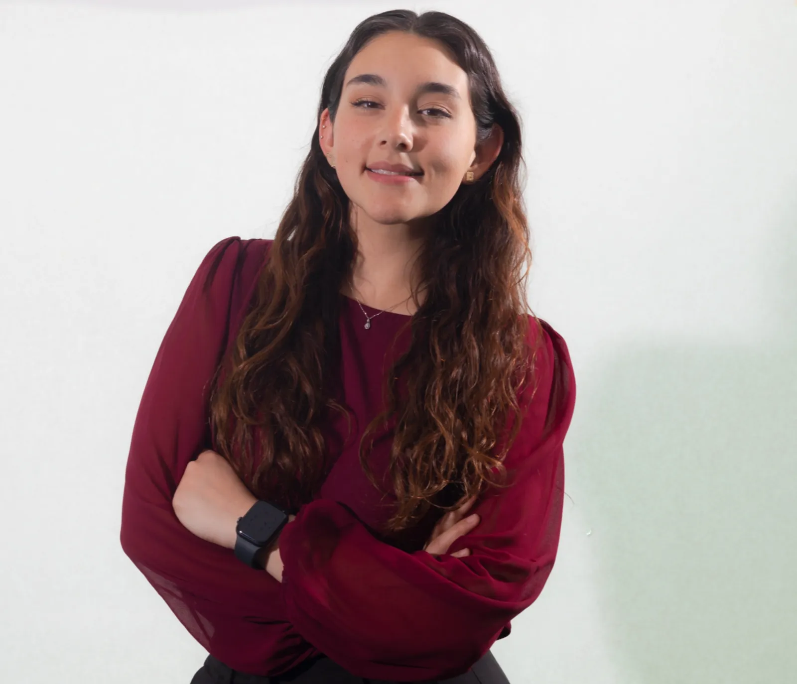 Woman in burgundy top with crossed arms and long wavy hair smiling