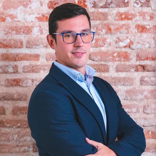 Professional man in blue jacket poses confidently against brick wall background