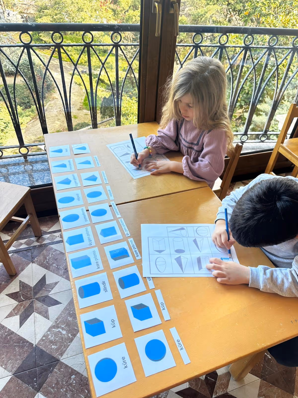 Montessori etkinliğinde çocuklar, üç boyutlu geometrik şekilleri eşleştirerek çizim çalışması yapıyor.