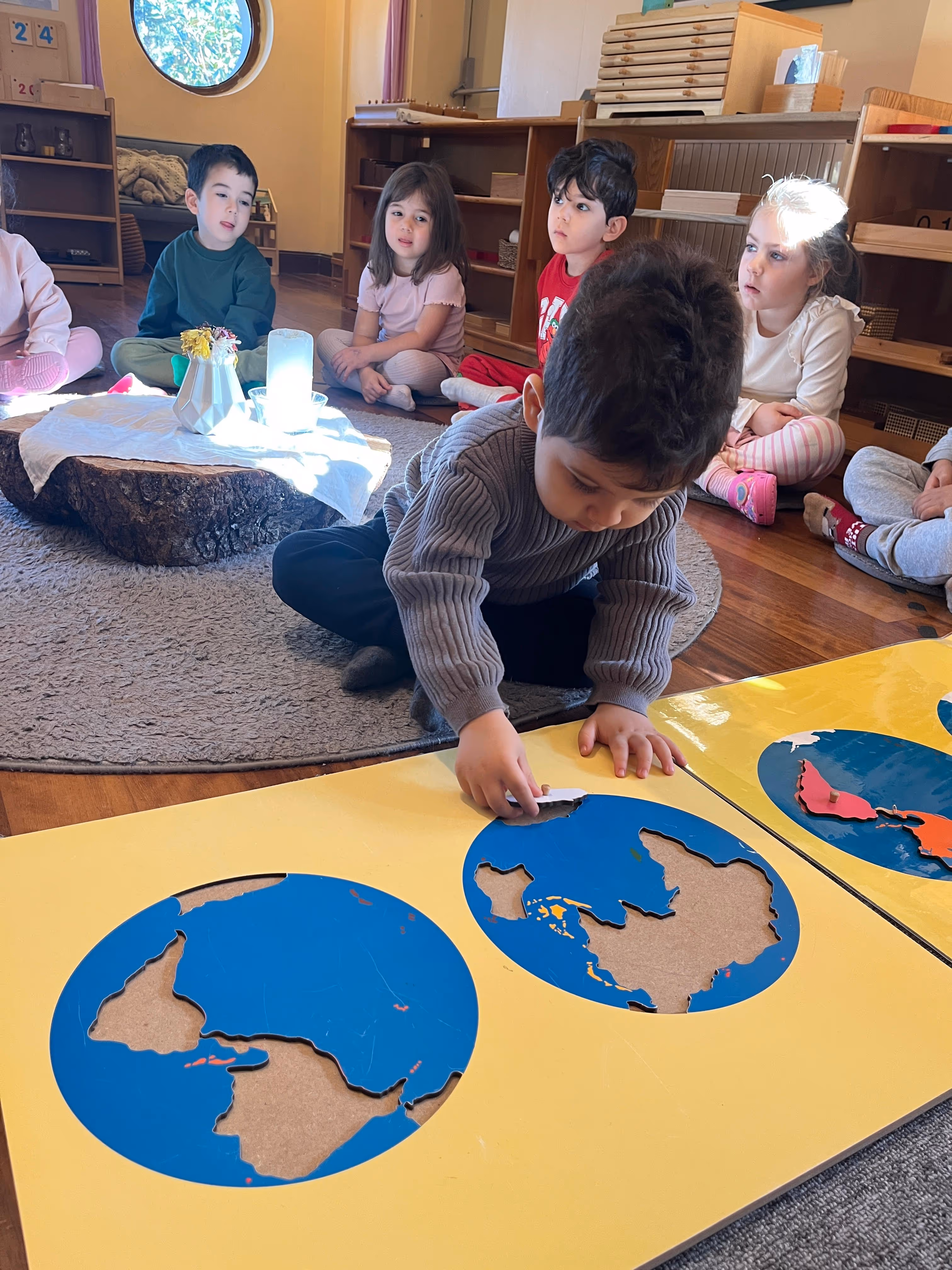 Montessori sınıfında bir çocuk, ahşap dünya haritası puzzle’ı ile kıtaları yerleştiriyor.