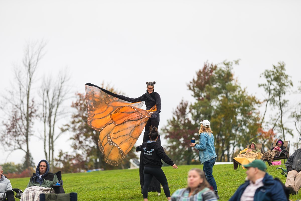 A costumed performer with large monarch butterfly wings on the festival lawn as families watch