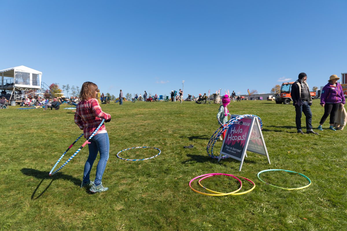 Festival-goers hula hooping on the grass beside a sign offering hoops free to borrow