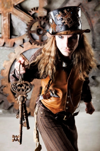 Man in steampunk style outfit with a tall top hat with tan detailing and featuring a tan waistcoat.  He holds out a bunch of large, old keys.