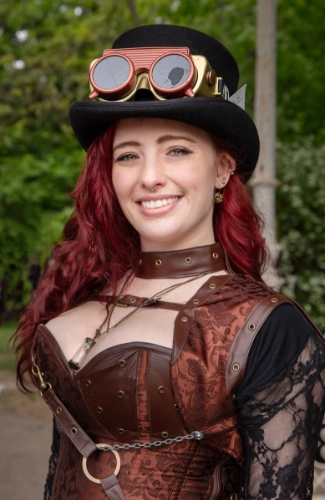Woman in steampunk style outfit with goggles around a top hat, and copper or light bronze bodice.
