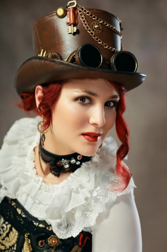 Woman in steampunk style outfit with goggles around a top hat, and a white chiffon top.