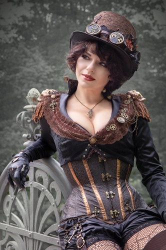 Woman in steampunk style outfit with goggles around a top hat, and a black corset with brown detailing over a black satin top.