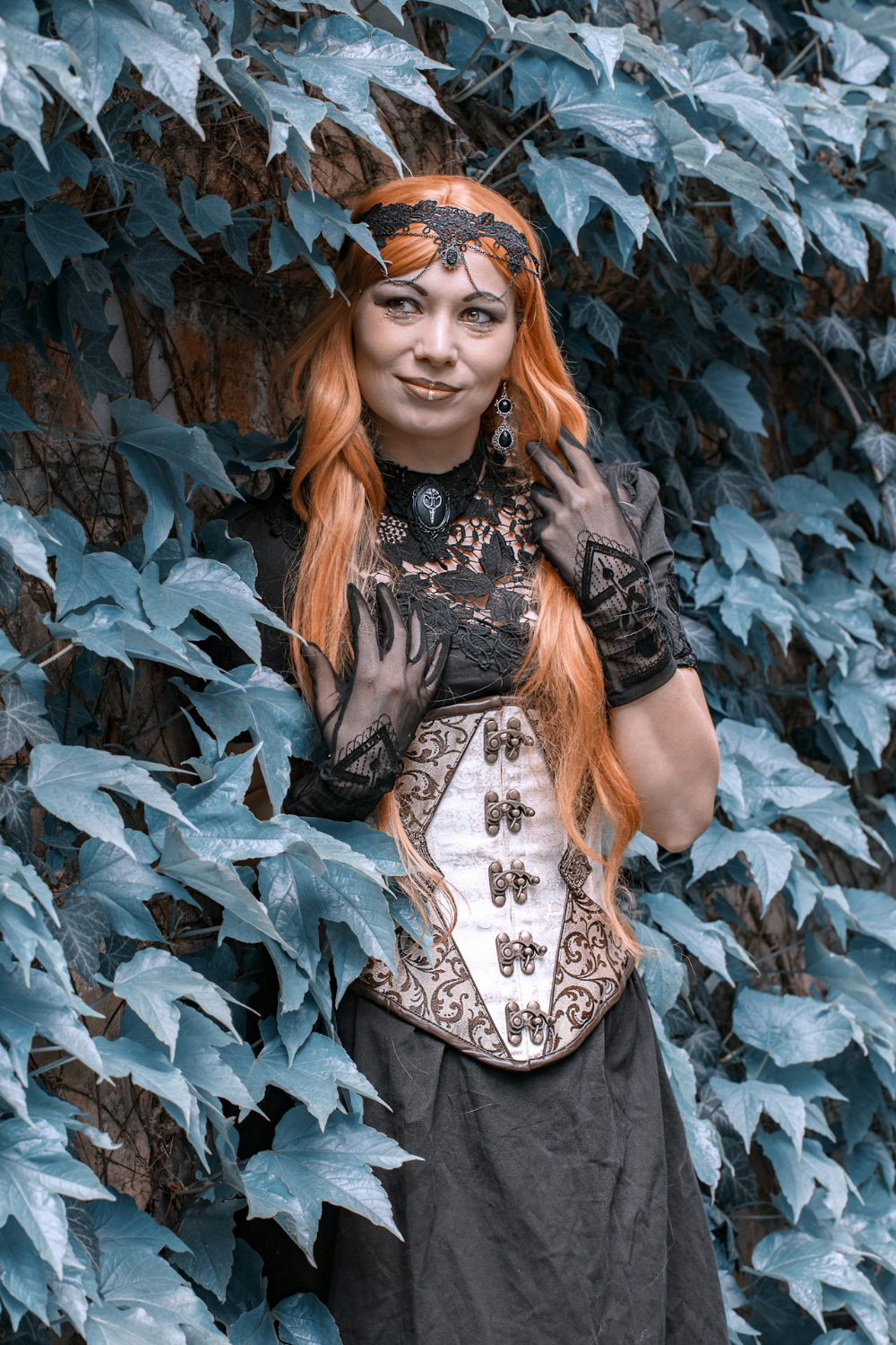 A lady in steampunk attire standing in front of a wall of ivy