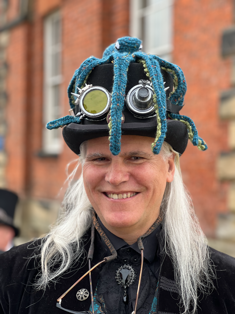 A man in steampunk attire wearing a top hat adorned with goggles and a crochet octopus