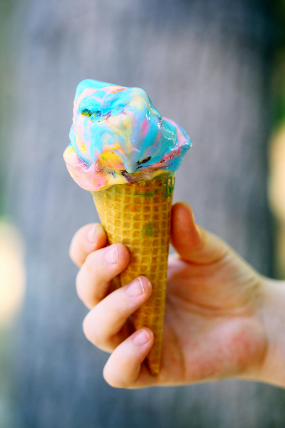 A child's hand holding a rainbow ice cream
