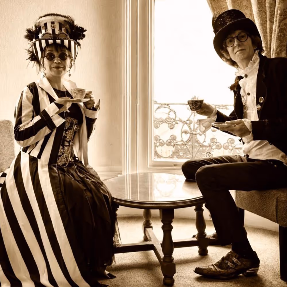 A sepia photo of a couple drinking tea in steampunk costumes.