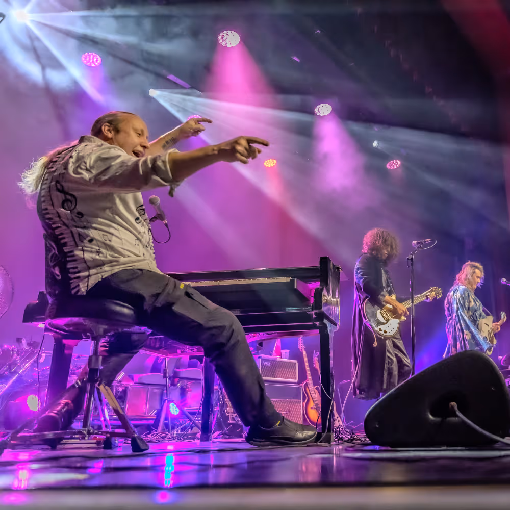 A man playing keyboard on a stage with purple lighting.