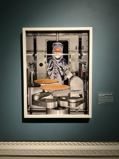 Photo of Lydia Fox gowned in the proper cleanroom attire peering into machine