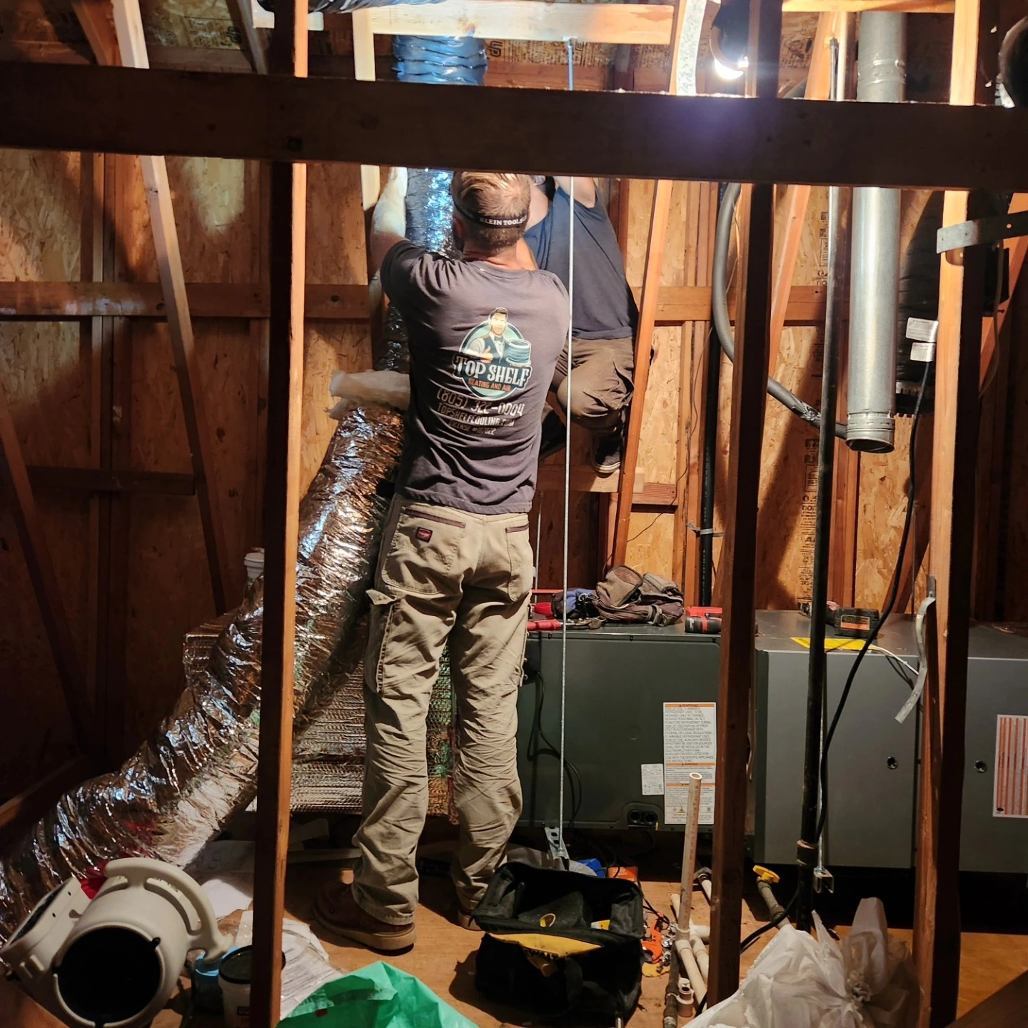 Worker in utility shirt installing equipment in mechanical room with pipes