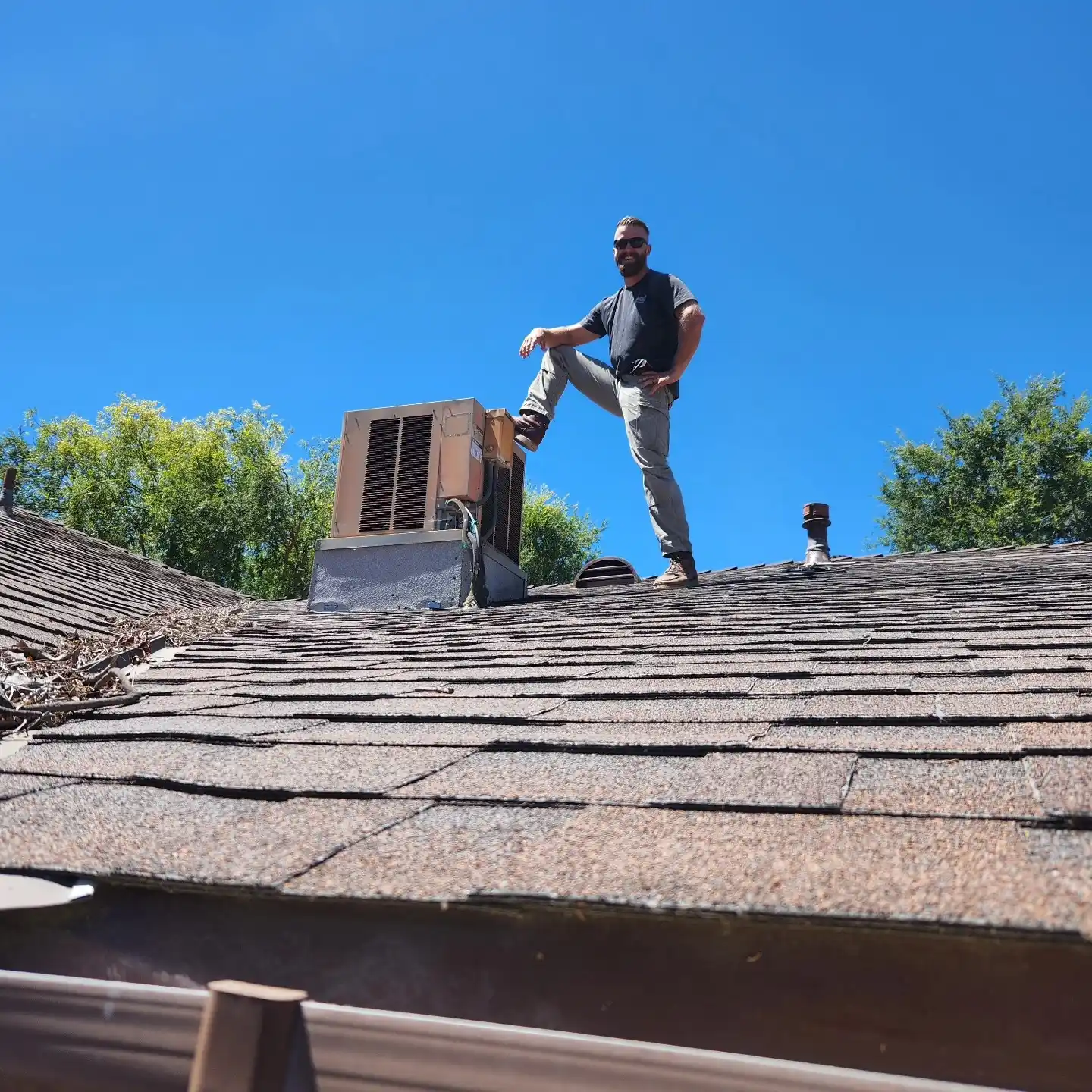 Person standing on old shingle roof near air conditioning unit on sunny day