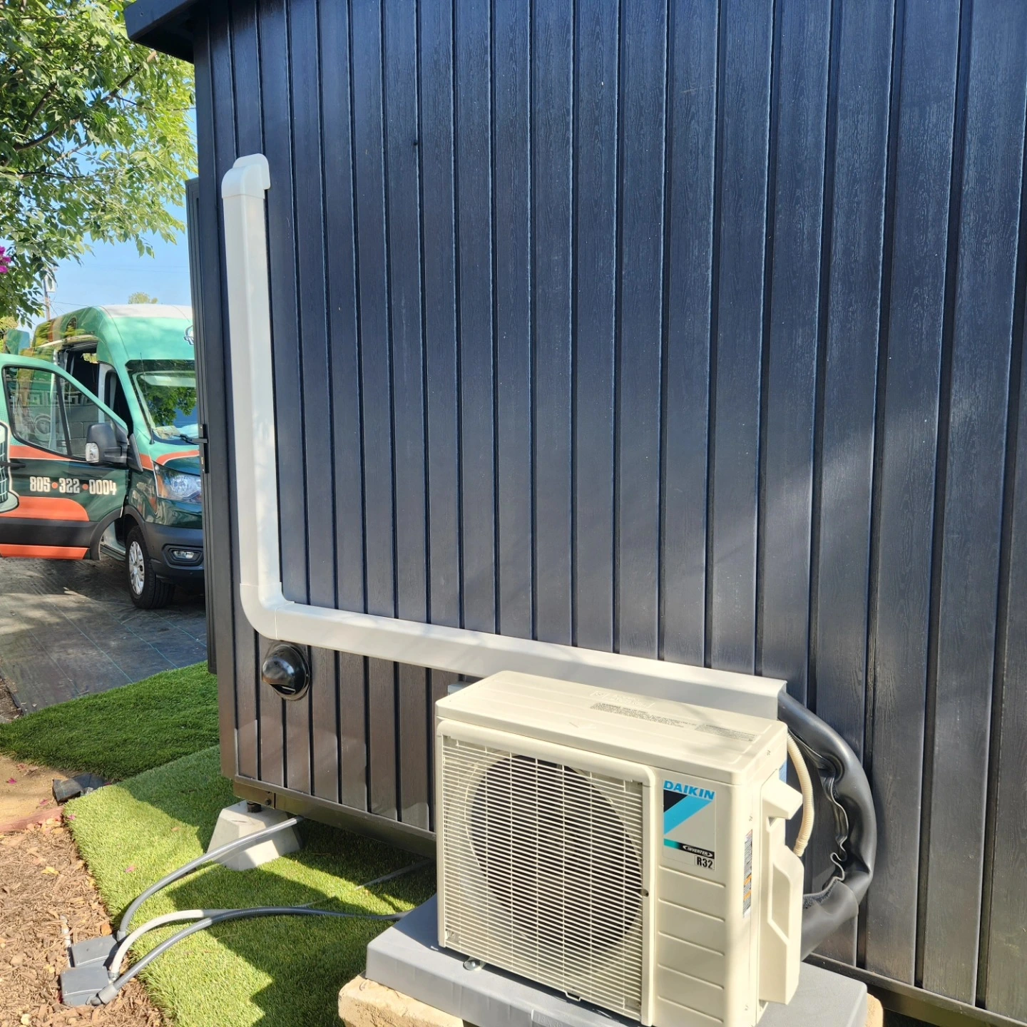 Daikin air conditioner unit mounted on blue-paneled wall near green van
