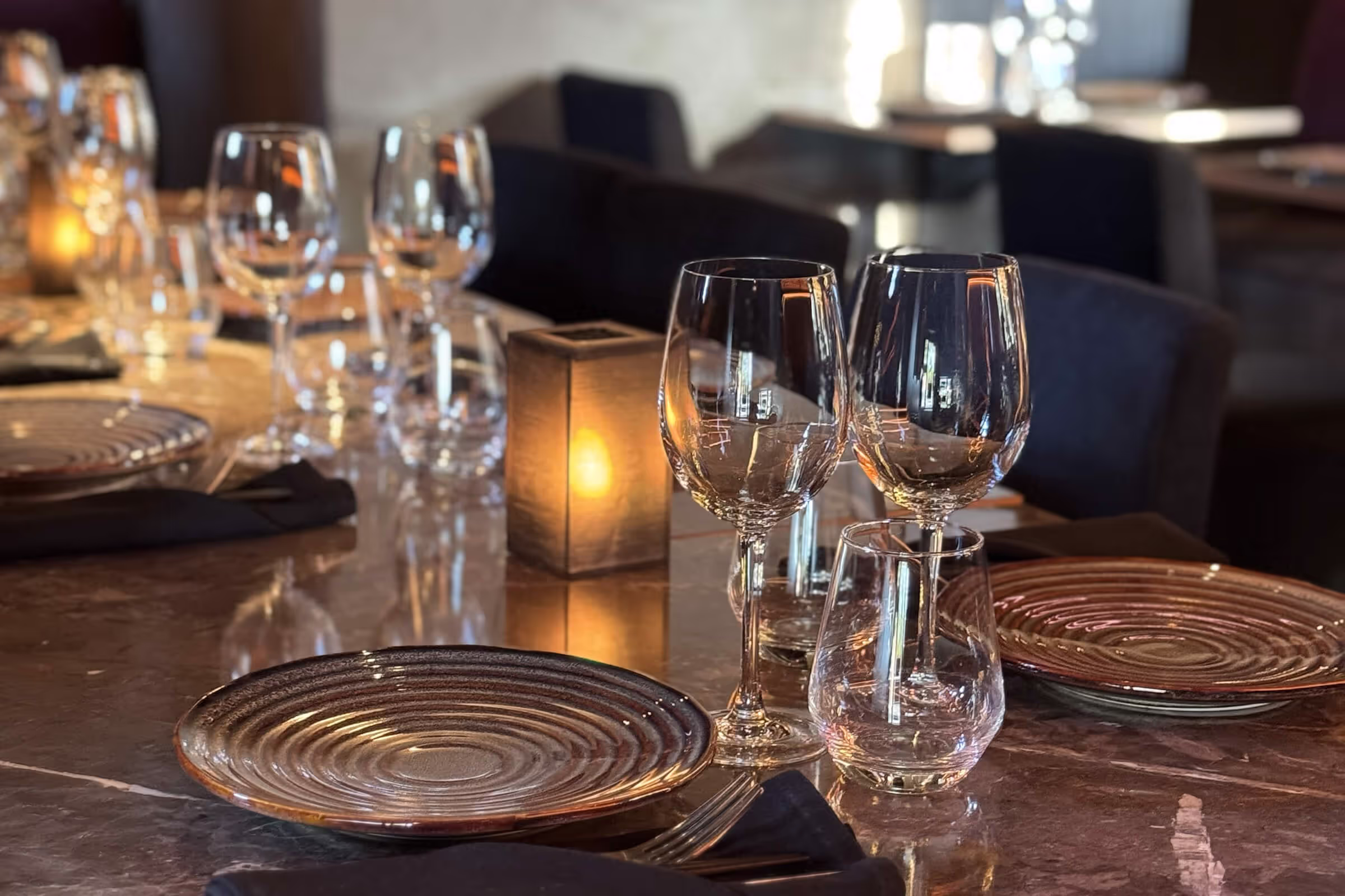 Mørkt marmorbord dekket med vinglass, tallerkner og tente lys. 
