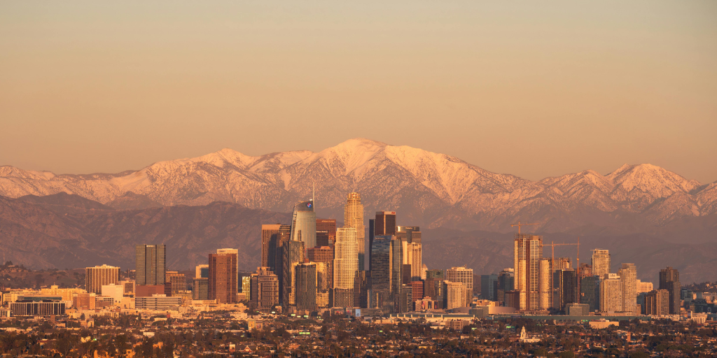 Downtown city skyline at sunset with mountain range, representing major metropolitan business district for security and risk management summit