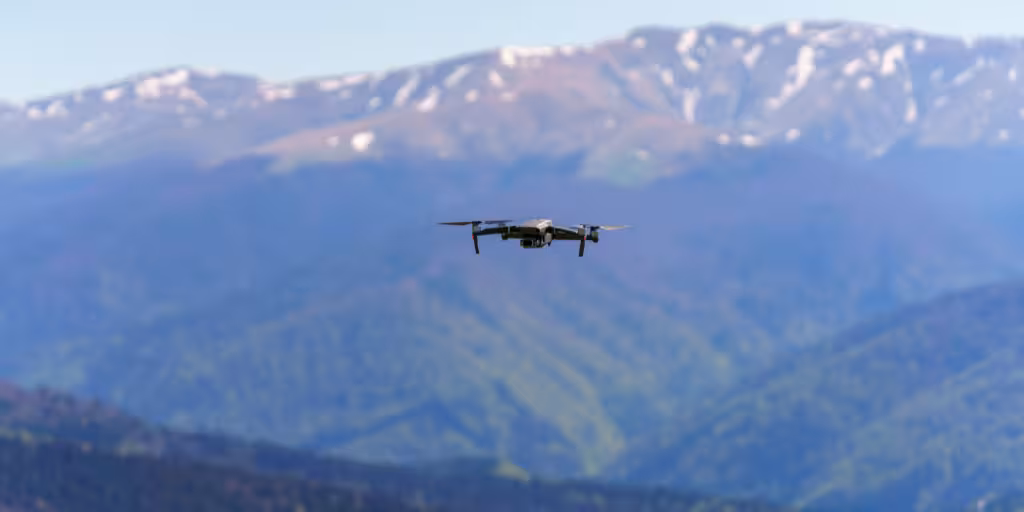 Small commercial drone flying over a vast mountain range with snowy peaks, illustrating modern drone technology used for environmental monitoring or infrastructure inspection.