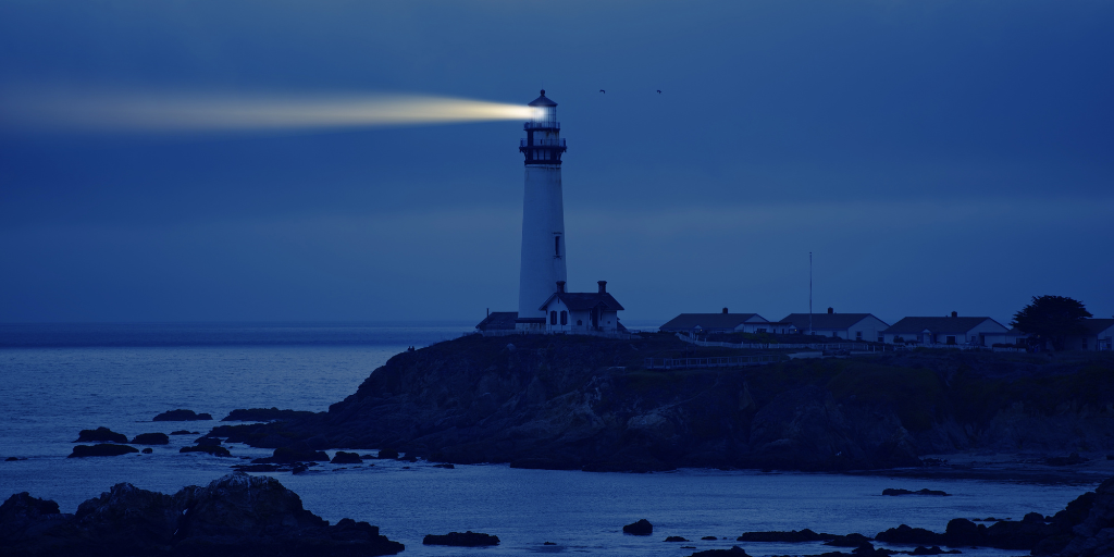 Coastal lighthouse providing early warning signals across the water at twilight.