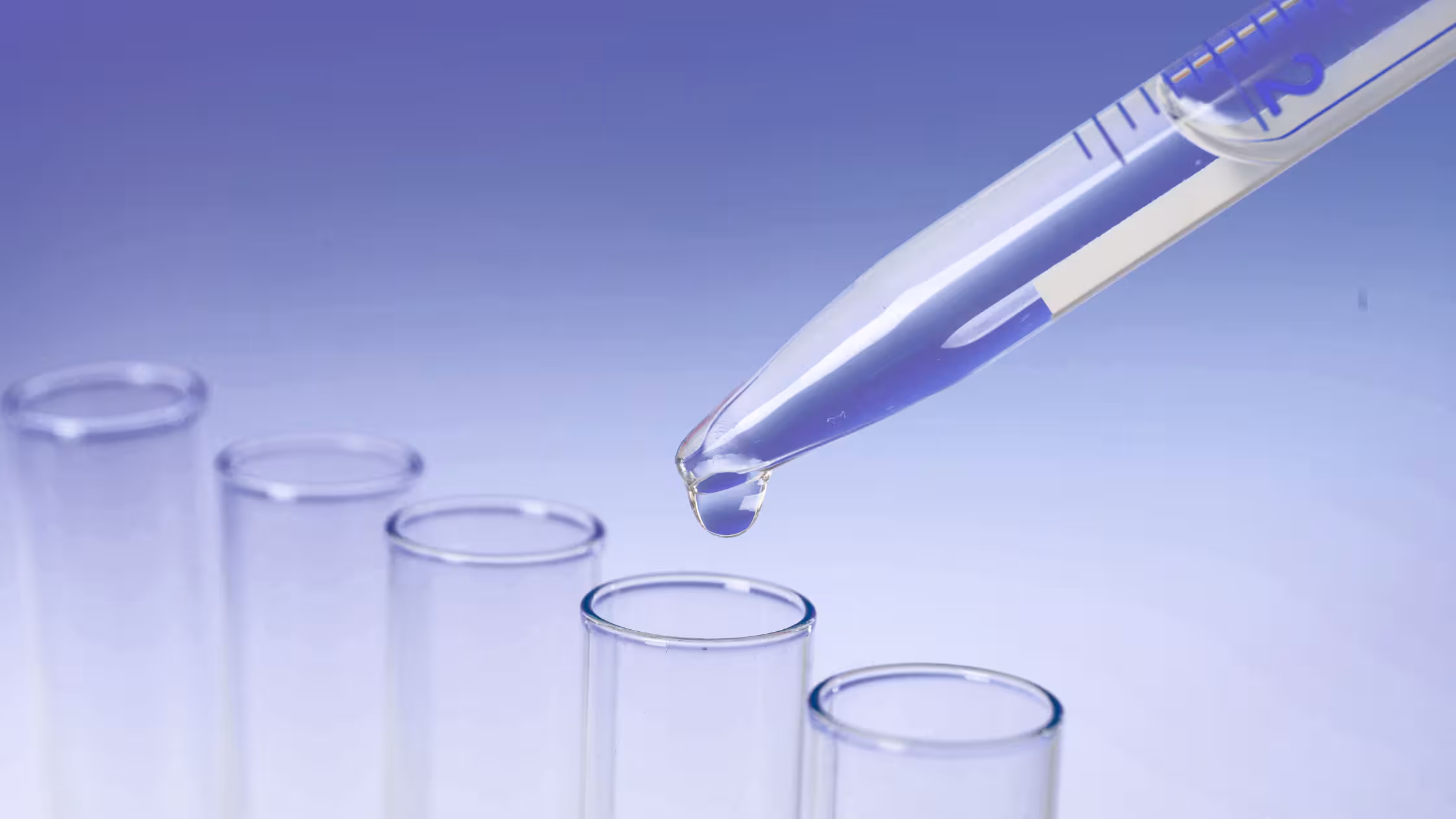 Close-up of a laboratory pipette dropping liquid into glass test tubes, representing the pharmaceutical development of semaglutide drugs like Ozempic.
