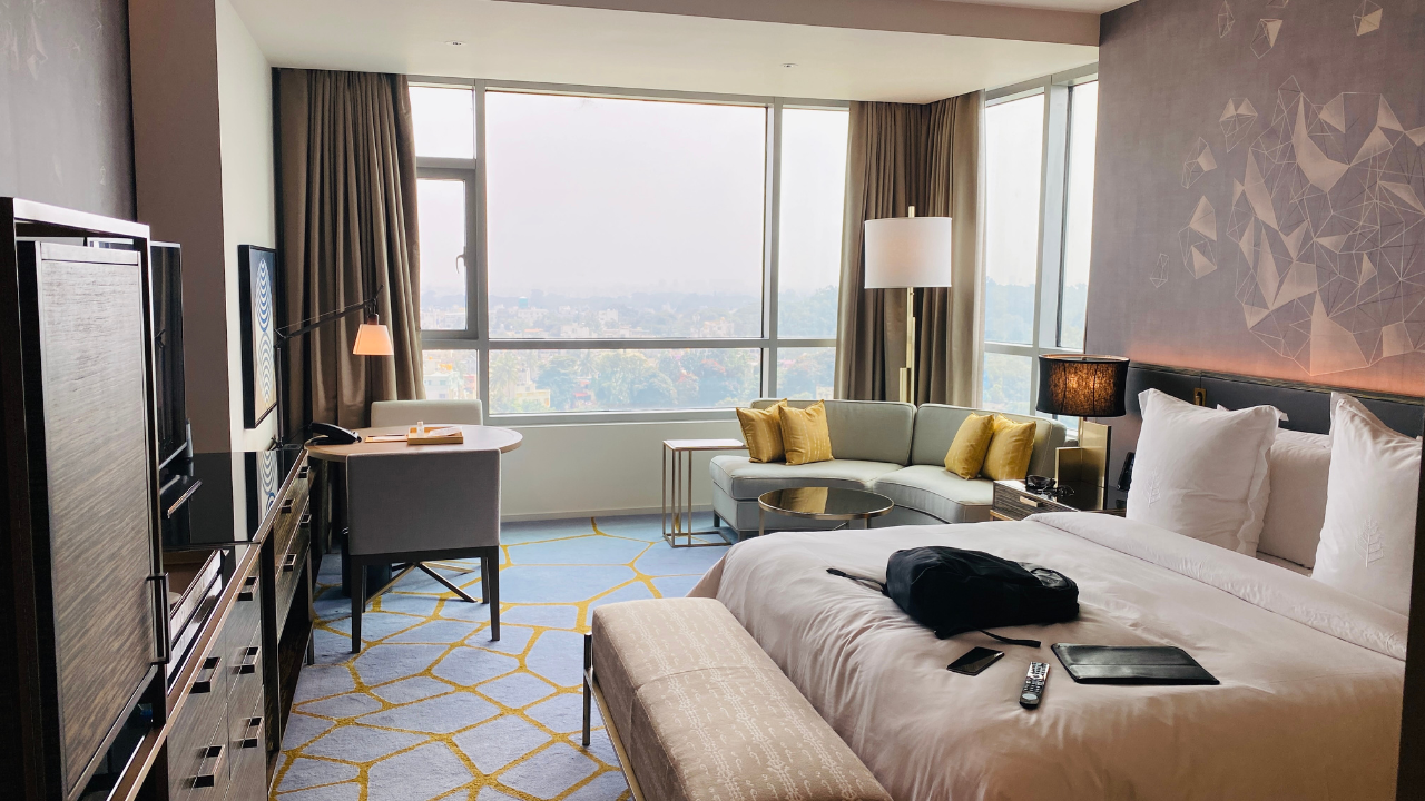 an expansive hotel room with an open curtain windows and a black bag on the bed