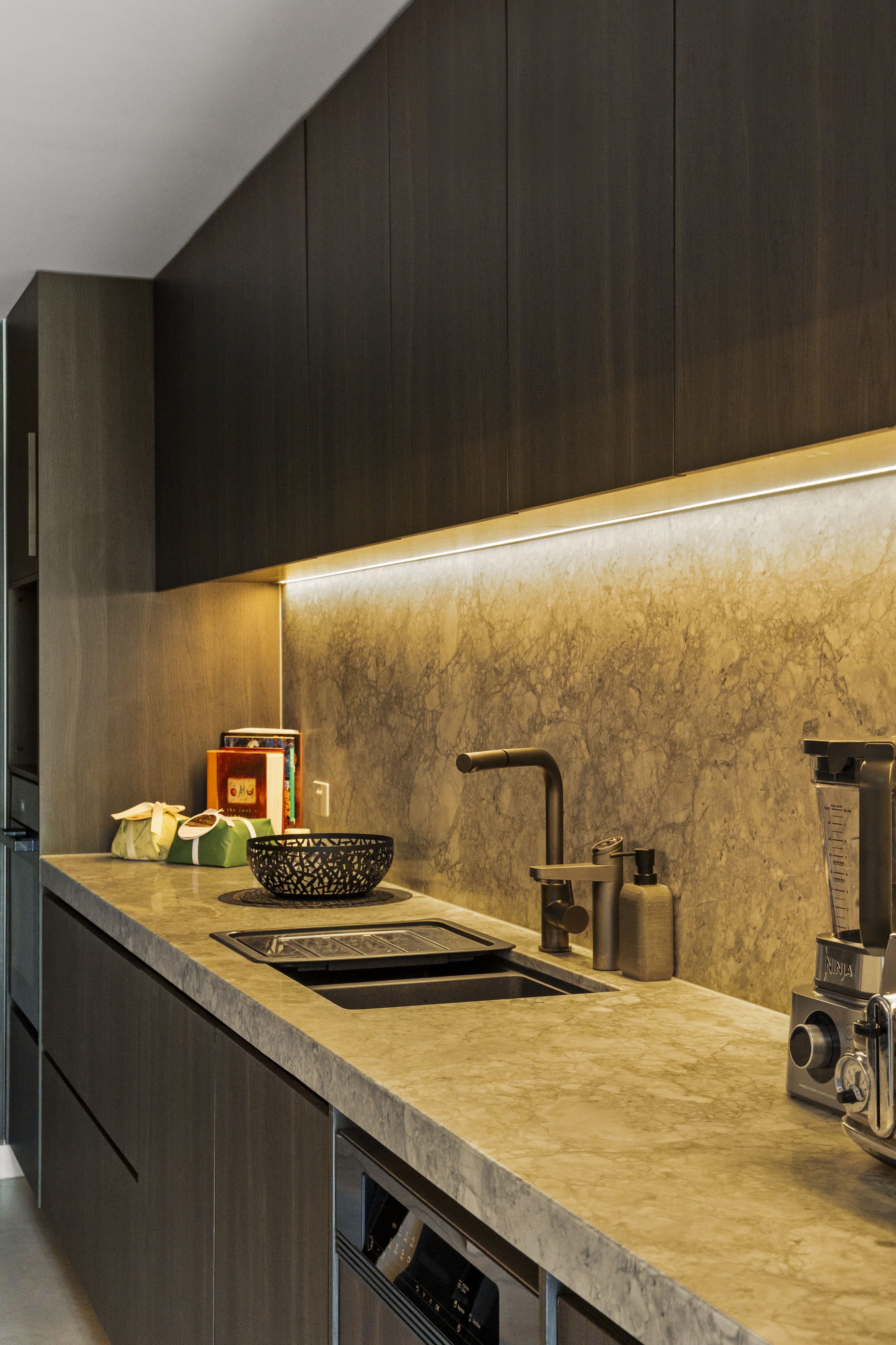 Modern kitchen countertop with dark cabinets, a built-in sink, a black bowl, soap dispenser, and a blender.