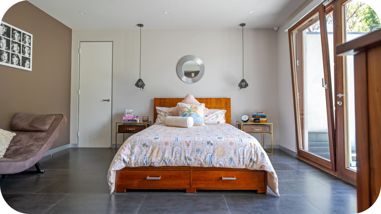A modern bedroom with dark grey tile floors, a wooden bed with storage drawers, and a large glass door opening to the outside.