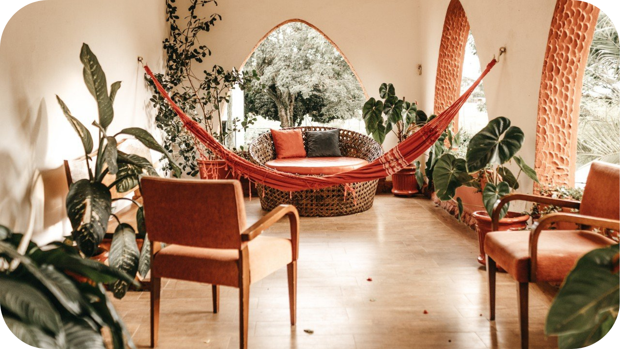 Mediterranean-inspired home interior with hammock, wicker furniture, arched windows, and lush indoor plants creating a cosy retreat.