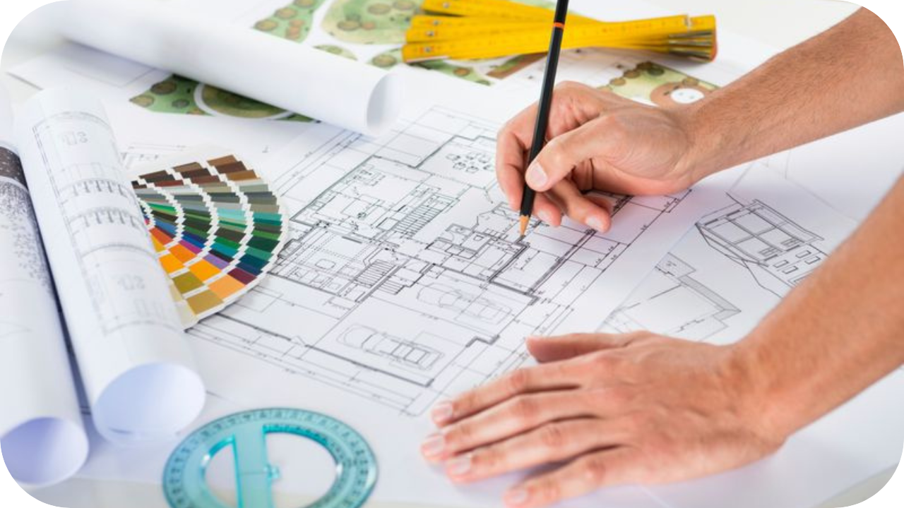 An architect’s desk with detailed floor plans, colour swatches, and drawing tools, as a hand sketches design elements on the blueprint.