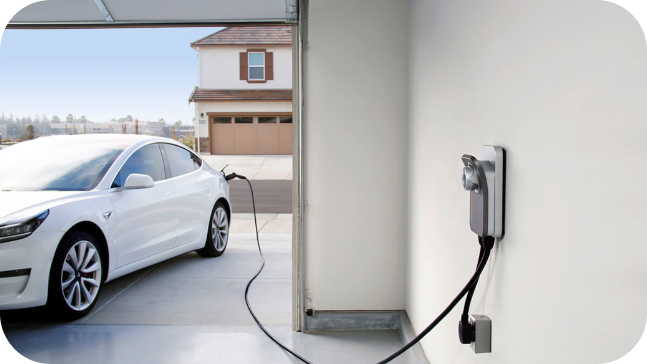 A white electric vehicle charging inside a home garage, connected to a wall-mounted residential EV charging station.