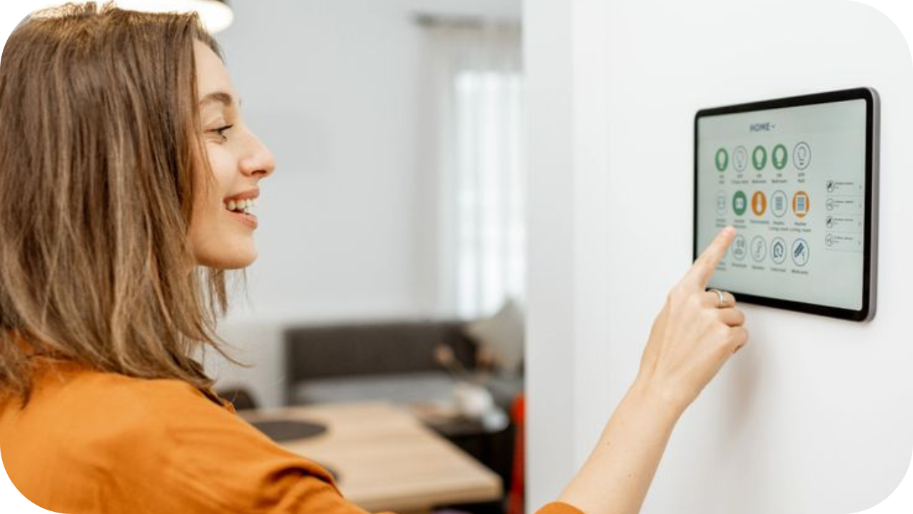 Smiling woman using a smart home control panel mounted on the wall to manage connected devices and home automation features.