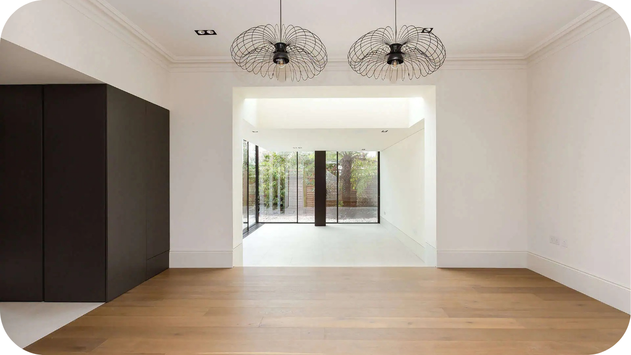 Minimalist living space with timber flooring, white walls, and modern black pendant lights near glass doors.