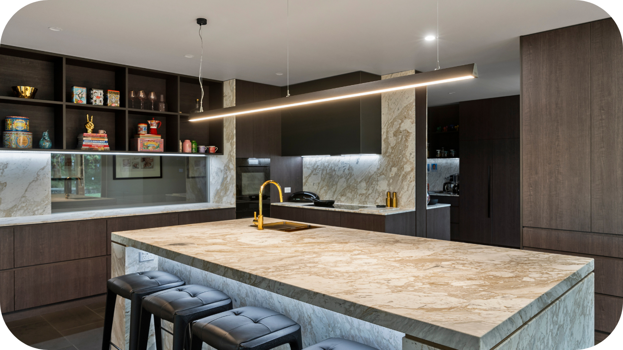 Contemporary kitchen with marble finishes, brass tapware, and a large island bench under modern pendant lighting.